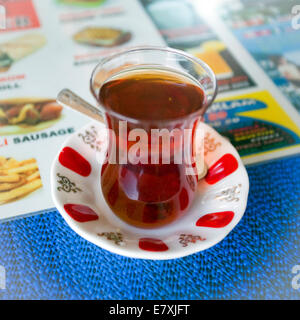 Un tè turco in tazza con piattino seduto su un menu e una tabella blu panno Foto Stock