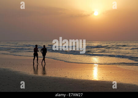 Due uomini jogging sulla spiaggia al tramonto, silhouette, Al-Batinah provincia, Oman, Penisola arabica Foto Stock