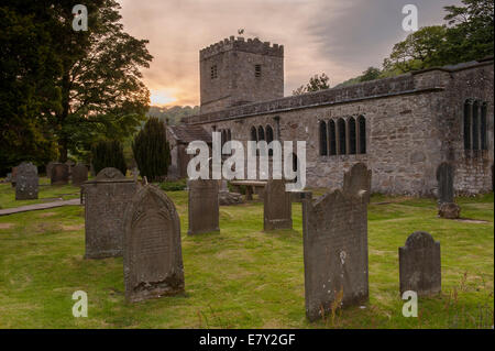 Esterno del San Michele e Tutti gli Angeli chiesa con lapidi nel cimitero sotto il cielo colorato al tramonto - Hubberholme, Yorkshire Dales, Inghilterra, Regno Unito. Foto Stock