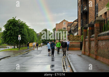 Rainbow alta in grigio cielo nuvoloso dopo improvviso rovescio di pioggia inzuppato & wet gente camminare su riverside road - York, North Yorkshire, Inghilterra, Regno Unito, Foto Stock