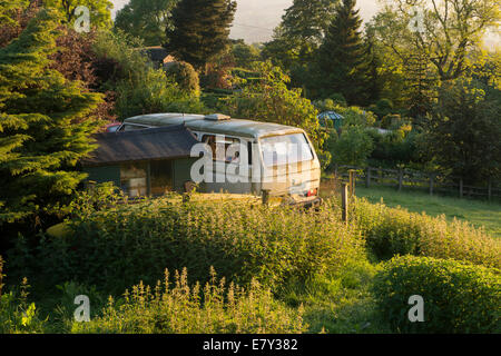Vecchio e sporco, trascurato, parcheggiato VW Camper Van sembra fuori luogo nella splendida e soleggiata e ben curato giardino - West Yorkshire, Inghilterra, Regno Unito. Foto Stock