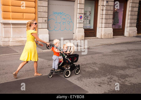 Donna cammina con i bambini in un passeggino in strada a Trieste Italia Foto Stock