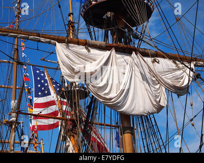 Cercando nel sartiame e piloni di Tall Ship, un arrotolato a vela, una grande bandiera americana e molte piccole bandiere internazionali Foto Stock