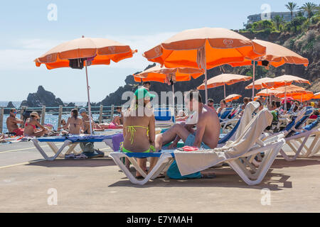 La gente seduta sotto un ombrellone in una piscina pubblica bagno a Madeira, Portogallo Foto Stock