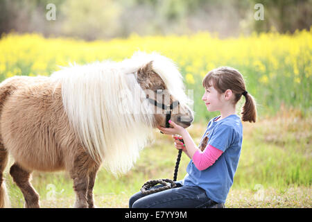 La ragazza (10-12) giocando con pony in Prato Foto Stock