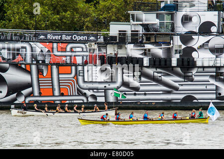 Barche di passare il dispositivo HMS Presidente che è stato verniciato in 'Dazzle' camuffamento di vernice in commemorazione di WW1, il grande fiume gara, London's River Marathon (noto anche come il Regno Unito barca tradizionale campionato) - Un 21,6 miglia gara in barca lungo il fiume Tamigi da Docklands di Londra al prosciutto in Surrey. Esso attrae oltre 300 equipaggi provenienti da tutto il mondo e fa appello ad ogni livello del concorrente di coloro che godono di divertimento, Fancy Dress e carità di acrobazie, a gravi sportivi. Il fiume Tamigi, Londra, 27 settembre 2014. Foto Stock