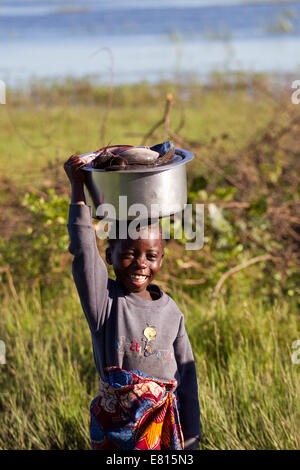 Un giovane bambino porta un secchio di pesce in un villaggio di pescatori in Bangweulu zone umide, Zambia Foto Stock