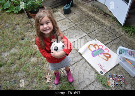 Sorridente ragazza tenendo palla calcio accanto a farfalla colore acqua opera d'arte al di fuori in giardino. Foto Stock