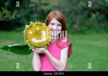 Ragazza con un girasole (Helianthus annuus) con una faccia sorridente Foto Stock