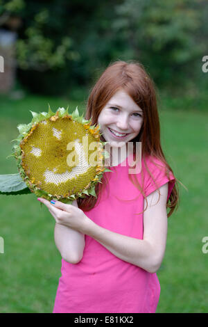 Ragazza con un girasole (Helianthus annuus) con una faccia sorridente Foto Stock