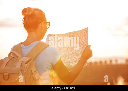 Lato posteriore della ragazza di viaggiatori alla ricerca giusta direzione sulla mappa, arancio brillante luce del tramonto, viaggiando lungo l'Europa, di libertà e di agire Foto Stock