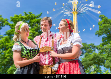 Le donne amici in visita bavarese festival folk in Dirndl in piedi di fronte a giostra Foto Stock