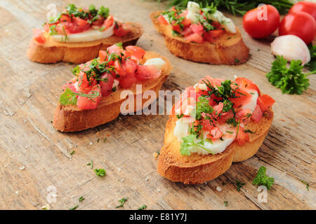 Antipasto fresco chiamato bruschetta con pomodoro, aglio, formaggio ed erbe su una tavola di legno Foto Stock