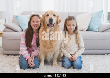 Sorelle seduta sul tappeto con il golden retriever sorridente in telecamera Foto Stock