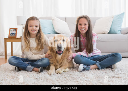 Sorridente sorelle petting loro golden retriever su rug Foto Stock