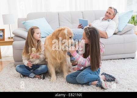 Sorridente sorelle petting loro golden retriever su rug Foto Stock