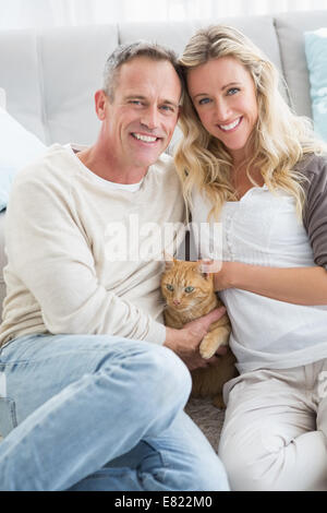 Coppia sorridente petting loro gringer cat su rug Foto Stock