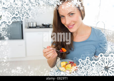 Sorridente giovane donna di mangiare insalata di frutta in cucina Foto Stock