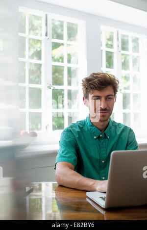 Un uomo seduto a un tavolo con un computer portatile. Lavorando da casa. Foto Stock