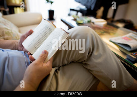 Uomo seduto sul divano a leggere un libro. Foto Stock