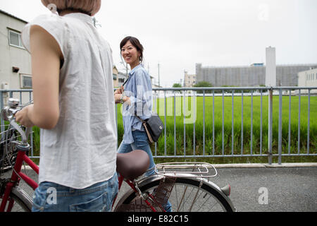 Due donne a piedi lungo un sentiero, spingendo una bicicletta. Foto Stock