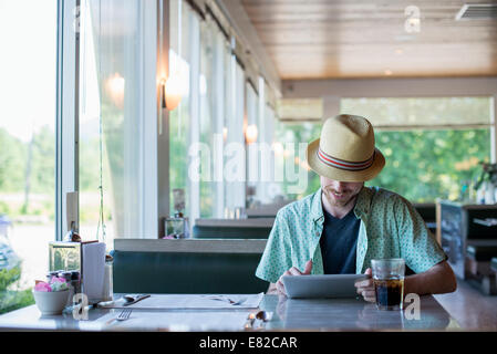 Un uomo che indossa un cappello seduti in un diner utilizzando una tavoletta digitale. Foto Stock