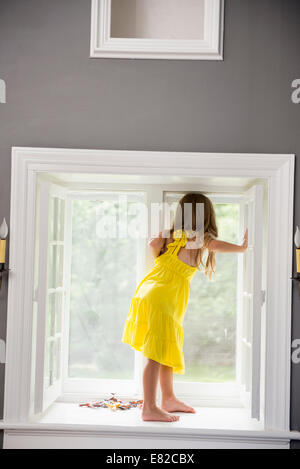 Una ragazza in un abito bianco posizionato da una finestra durante la riproduzione. Foto Stock