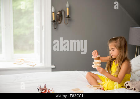 Una ragazza seduta su di un letto, giocando con blocchi di costruzione. Foto Stock