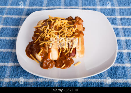 Due cani a caldo su una piastra bianca soffocato in carni bovine di peperoncino e di formaggio Cheddar grattugiato Foto Stock