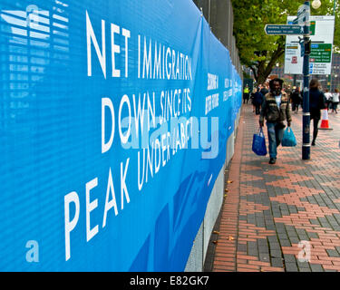 Birmingham, Regno Unito 29/09/2014. Un uomo di discesa dei Caraibi passeggiate passato un conservatore slogan circa il partito della limitazione dell'immigrazione presso il congresso del Partito Conservatore 2014, Birmingham (C) Paolo Swinney/Alamy Live News Foto Stock