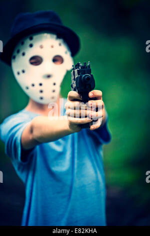Ragazzo mascherato mirando con pistola giocattolo Foto Stock