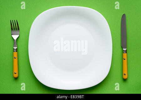 Bianco piastra vuota con coltello e forchetta sulla tovaglia verde Foto Stock