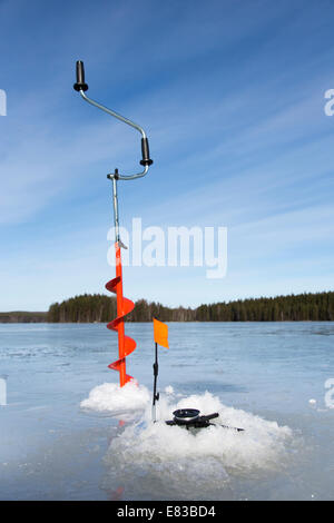 La trivella di ghiaccio e la canna da pesca del ghiaccio di punta sul lago congelato a Winter , Finlandia Foto Stock