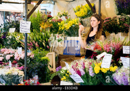 Una fiorista donna nella sua bancarella di fiori che vende fiori al mercato di Cambridge, Cambridge, Inghilterra, Regno Unito Foto Stock