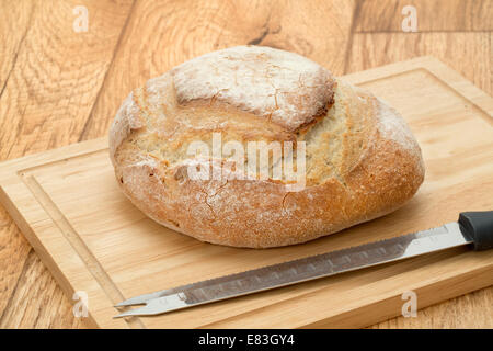 Un rustico francese pagnotta di pane su un tagliere di legno con un coltello per pane - studio shot Foto Stock