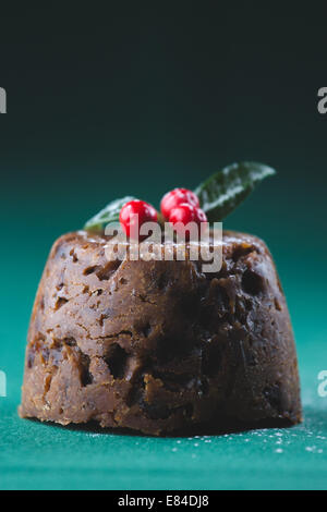 Pudding natalizio vestito con l'inverno bacche e foglie e spolverato con zucchero a velo Foto Stock