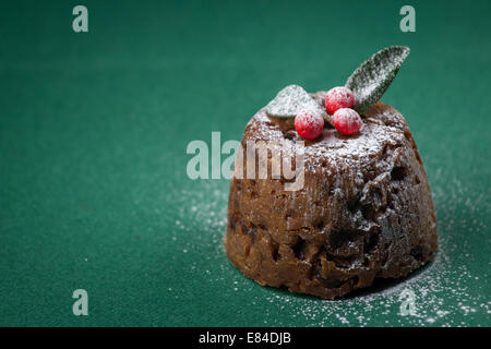 Pudding natalizio vestito con l'inverno bacche e foglie e spolverato con zucchero a velo Foto Stock