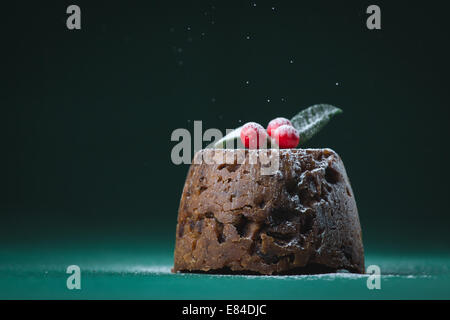 Pudding natalizio vestito con l'inverno bacche e foglie e spolverato con zucchero a velo Foto Stock