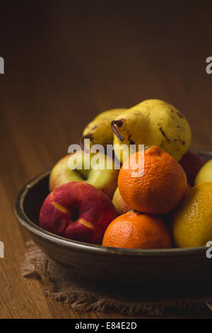 Una coppa di frutta illuminato da sparare attraverso ombrello di un tavolo di legno Foto Stock