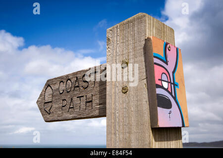 Regno Unito, Inghilterra, Devon, Putsborough, sentiero costiero segno con graffiti illustrazione attaccata Foto Stock