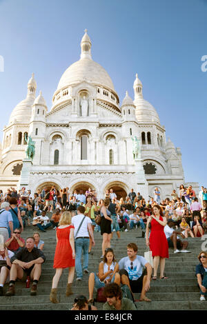 Persone - turisti che si siedono sui gradini della chiesa del Sacro Cuore di sera, Montmartre, Paris, Francia Europa Foto Stock