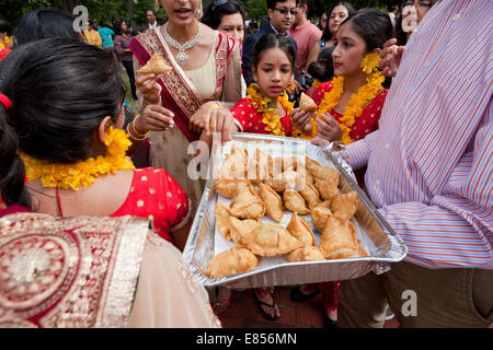 Folla di persone raccolte intorno ad una piastra di indiani Samosa Foto Stock