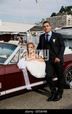 Sposa e lo sposo in posa con un open ford mustang convertible auto presso un porto Foto Stock