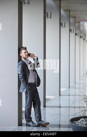 Giovane dirigente tenendo chiamata mentre appoggiata contro la colonna nella lobby di costruzione Foto Stock