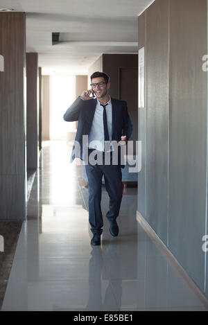Giovane imprenditore parlando al telefono mentre passeggiate attraverso office Foto Stock