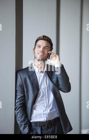 Giovane uomo appoggiato a colonna edili parlando al cellulare Foto Stock