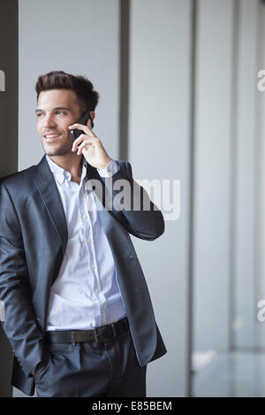 Giovane uomo appoggiato a colonna edili parlando al cellulare Foto Stock