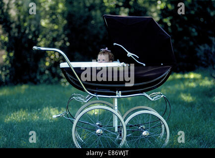 Un elegante vintage inglese pram acquistato da Harrods a Londra è stata fotografata nel 1971 con una piccola bambina peeking oltre il bordo del suo carrello. È stata parcheggiata in ombra nella speranza che lei sarebbe ottenere sonnolenta e schiacciare un pisolino. La classica pram featured linee eleganti, sospensione morbida, grandi ruote con pneumatici in gomma, una cappa di piegatura, e un elegante interno imbottito. Foto Stock