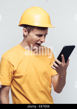 L'uomo lavoratore in un casco guarda tablet pc Foto Stock