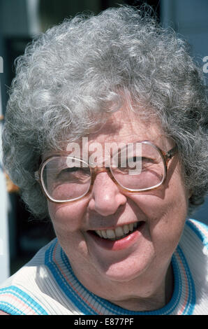 Un anziano di 70-anno-vecchio American Caucasian donna con i capelli grigi e grandi occhiali bifocali sorride al sole luminoso per un informale di close-up verticale Foto Stock